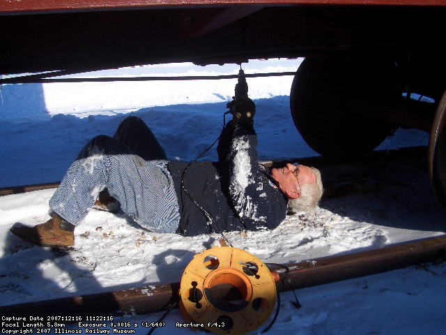 12.16.07 - 13 DEGREES WITH SIX INCHES OF SNOW.  WORK CONTINUES IN SPITE OF THE WEATHER.  KIRK WARNER IS DRILLING PILOT HOLES TO COMPLETE THE INSTALLATION OF THE TIMBER BOLTS SECURING THE DECKING TO THE CENTERSILL ON THE B END OF THE CAR.
