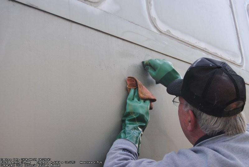 Close-up of Kevin working to remove adhesive on the 1st Exhibit Car exterior