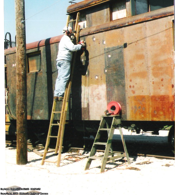 09.10.04 - THE LEFT SIDE OF THE CAR HAS BEEN NEEDLE CHIPPED TO REMOVED THE OLD PAINT.  KIRK WARNER IS WIRE WHEELING THE METAL PRIOR TO APPLYING PRIMER.