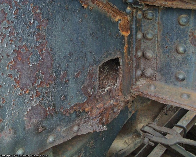 A BODY BOLSTER VERTICAL WEB HAS A HOLE CUT IN IT, PROBABLY AT THE REFINERY TO ALLOW FOR WATER TO DRAIN.  THE INSIDE OF THE BODY BOLSTER IS FULL OF RUST AND PRODUCT RESIDUE.