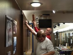 Mark marking the location for a bracket to hold the top of the new display cabinet while Jon is holding the top of the cabinet - Photo by Brian LaKemper